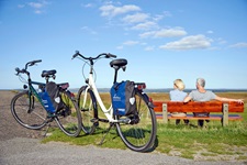 Ein Paar macht gemütlich auf einer Bank Pause und schaut über die Nordsee, im Vordergrund stehen die geparkten Fahrräder der beiden.