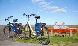Ein Paar macht gemütlich auf einer Bank Pause und schaut über die Nordsee, im Vordergrund stehen die geparkten Fahrräder der beiden.