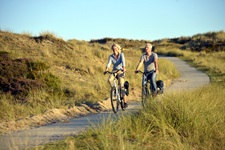 Ein Radlerpärchen folgt einem von Dünen gesäumten Radweg durch Nordfriesland.