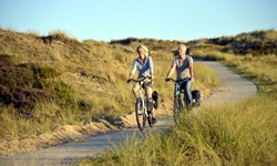 Ein Radlerpärchen folgt einem von Dünen gesäumten Radweg durch Nordfriesland.