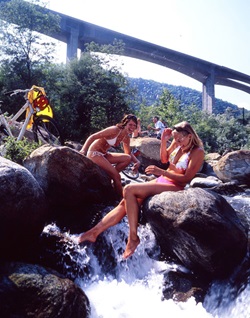 Zwei junge Frauen im Bikini sitzen auf zwei Steinen im Fluss Ticino und erfrischen sich.
