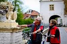 Ein Radlerpärchen bewundert die Löwenstatue vor dem Wasserschloss von Dornum.