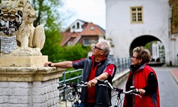 Ein Radlerpärchen bewundert die Löwenstatue vor dem Wasserschloss von Dornum.