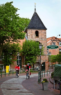 Zwei Radler fahren an der Kirche von Greetsiel vorbei.