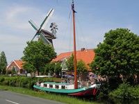 Ein Flussschiff fährt an einer ostfriesischen Windmühle vorbei.