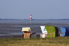 Bunte Strandkörbe bei Dangast, im Hintergrund der von Wasser umgebene Leuchtturm von Arngast.