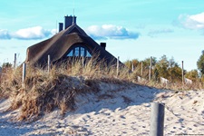 Ein reetgedecktes Haus überragt eine Düne an der Ostseeküste.