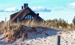 Ein reetgedecktes Haus überragt eine Düne an der Ostseeküste.