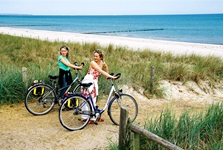 Zwei Frauen schieben ihre Räder über einen Deich an den Strand