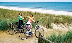 Zwei Frauen schieben ihre Räder über einen Deich an den Strand