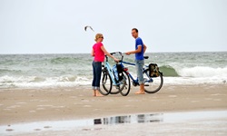 Zwei Radler stehen barfuß am Strand der Ostsee neben ihren Rädern