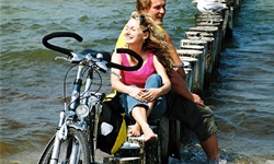 Zwei Personen sitzen auf Holzpflöcken an der Ostsee - neben ihnen steht ein Fahrrad