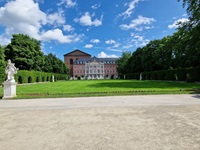 Der gepflegte Palastgarten, umrandet von einigen Statuen mit dem Palais von Trier