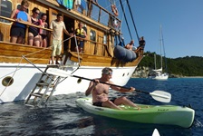 Ein Passagier probiert eines der Kanus aus, die zur Ausrüstung der Panagiota gehören. Andere Passagiere schauen ihm vom Schiff aus zu.