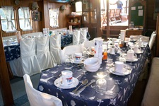 Ein schön eingedeckter Frühstückstisch mit weißem Geschirr auf blauer Tischdecke mit weißem Muster wartet im Salon der Panagiota auf die ersten Frühaufsteher.