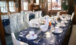 Ein schön eingedeckter Frühstückstisch mit weißem Geschirr auf blauer Tischdecke mit weißem Muster wartet im Salon der Panagiota auf die ersten Frühaufsteher.