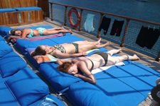 Drei Frauen im Bikini genießen auf den blauen Liegematten, mit dem das Sonnendeck der Panagiota ausgestattet ist, die Sonne.