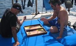 Zwei junge Männer spielen auf einer der blauen Liegematten, mit denen das Sonnendeck der Panagiota ausgelegt ist, eine Partie Backgammon.