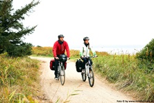 Zwei Radfahrer fahren auf einem befestigten Sandweg durch die Landschaft an der Küste Dänemarks entlang