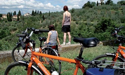 Zwei Radlerinnen genießen von einer kleinen Mauer aus die herrliche toskanische Landschaft.