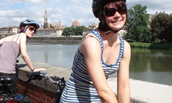Zwei Radlerinnen machen am Arno eine kurze Pause, im Hintergrund die Silhouette von Florenz mit der Kuppel des Doms "Santa Maria del Fiore".
