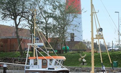 Zwei Boote sind an einem kleinen Hafen am Nordseeküsten-Radweg angelegt, im Hintergrund ist ein rot-weißer Leuchtturm zu sehen