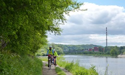 Zwei Radfahrer mit gelben Warnwesten radeln auf dem Elbe-Radweg am Flussufer entlang.
