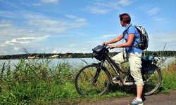 Eine Radlerin steht am Rand der Rhone und blickt in die Landschaft