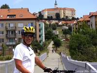 Ein Fahrradfahrer steht auf einer Brücke in Mikulov in Tschechien - im Hintergrund ist das gleichnamige Schloss zu sehen