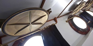 Detailbild von drei geöffnetet Bullaugen mit aufgezogenen dunkelblauen Vorhängen der MS Princesse Royale