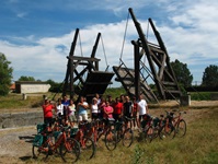 Eine Gruppe Radreisender steht hinter ihren abgestellen Rädern vor einer hölzernen Klappbrücke