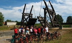 Eine Gruppe Radreisender steht hinter ihren abgestellen Rädern vor einer hölzernen Klappbrücke