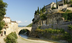 Steinbrücke bei einem in Ockertönen gehaltenen und damit typisch provenzalischen Dorf.