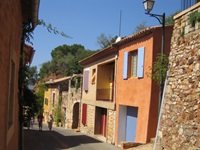 Zum Schlendern einladende Gasse mit ockerfarbenen Häuserfronten in einem typisch provenzalischen Dorf.