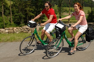 Eine Frau und ein Mann radeln auf einem Radweg entlang - im Hintergrund ist ein Fluss zu erkennen