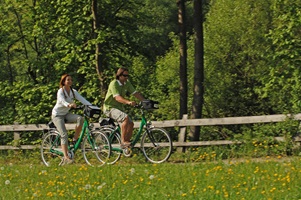 Ein Radlerpaar radelt auf einem Radweg im Grünen an einem Holzzaun vorbei