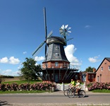 Zwei Radfahrer fahren auf einer Straße auf Föhr an einer Windmühle vorbei