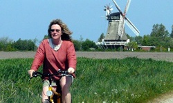 Eine Fahrradfahrerin fährt auf einem Schotterweg in Nordfriesland entlang, im Hintergrund ist eine Windmühle zu sehen