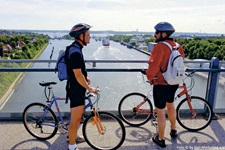 Zwei Radfahrer stehen auf einer Brücke bei der Radreise Ostseeküste und Holsteinische Schweiz und sie blicken auf den Kanal mit Schiffen