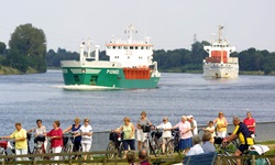 Eine Gruppe Radfahrer auf dem Radweg am Nord-Ostsee-Kanal - auf dem Kanal sind zwei Schiffe zu sehen