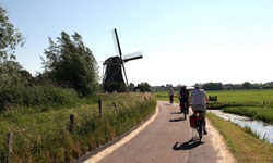 Eine Radlergruppe fährt auf einem Radweg zwischen Wasser und einer Mühle vorbei
