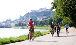 Eine Gruppe Radfahrer auf einem asphaltierten Radweg bei Salzburg. Im Hintergrund ist die Skyline der Mozartstadt zu erkennen.