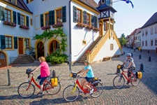 Drei Radfahrer passieren das Rathaus von Deidesheim.