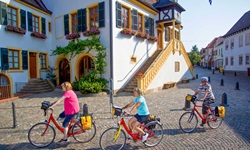 Drei Radfahrer passieren das Rathaus von Deidesheim.