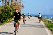Mehrere Radler fahren auf einer Straße am Meer entlang.