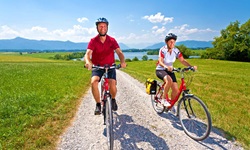 Zwei Radler sind auf einem weiß gekiesten Radweg im bayerischen Fünf-Seen-Land unterwegs.