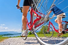 Zwei Radler fahren im bayerischen Voralpenland auf einen See zu.