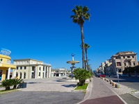 Eine breite, von Palmen gesäumte Straße in Viareggio führt auf den mit einem Pferd geschmückten Vier-Jahreszeiten-Brunnen von Giuseppe Domenici zu.