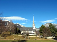 Blick auf einen Spielplatz und eine Kirche - im Hintergrund sind einige schneebedeckte Berggipfel zu
