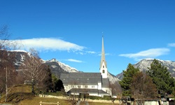 Blick auf einen Spielplatz und eine Kirche - im Hintergrund sind einige schneebedeckte Berggipfel zu
